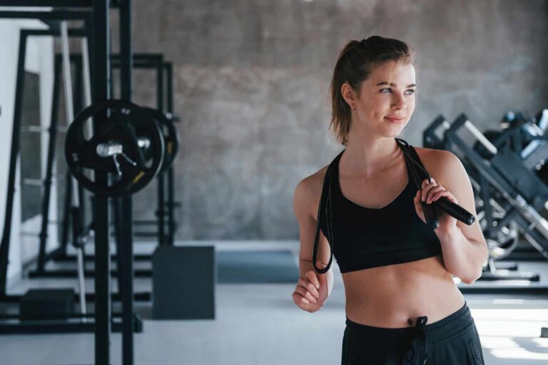 Woman in sports bra holding jump rope in gym looks to the side.